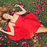 15871951 – beautiful young woman lying on grass with flowers in red dress
